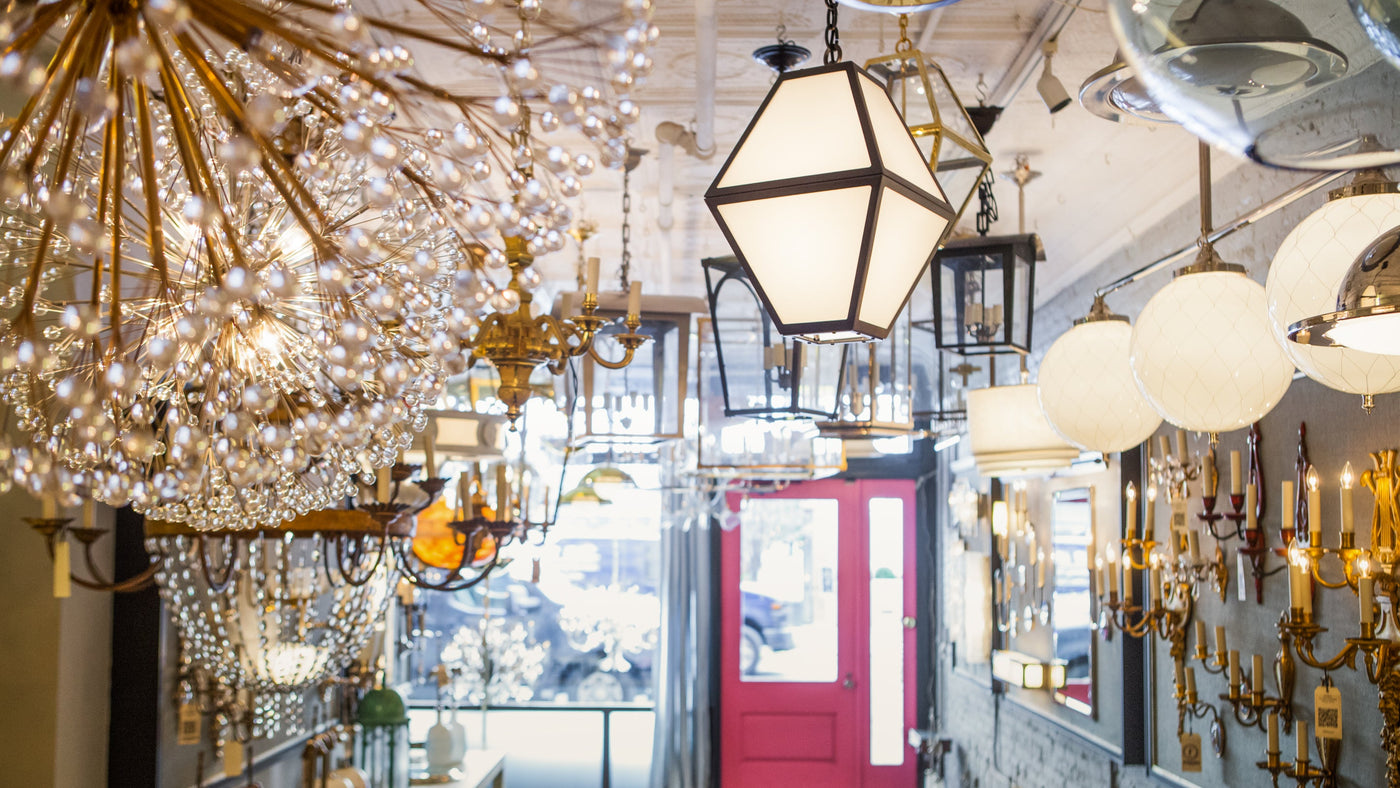 An interior view of the Remains Lighting Co. flagship showroom, filled with our signature lighting fixtures, and facing the pink front door and window out to the flower block in Manhattan.