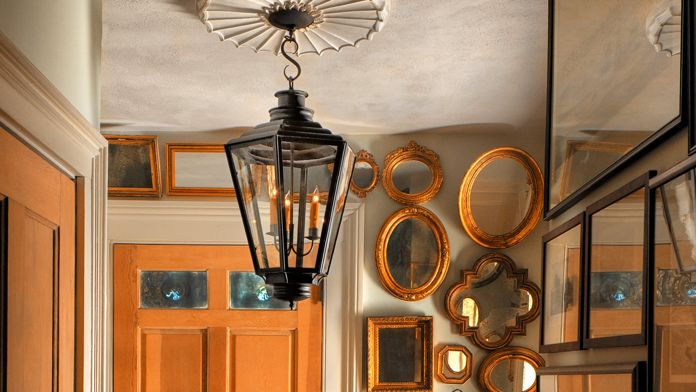A Scofield Lighting English Gas Exterior Lantern hangs inside an entryway with gilt framed mirrors surrounding the front door from floor to ceiling.