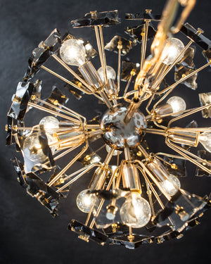 A detail view of a vintage sputnik form Fontana Arte chandelier with smoke glass elements in a warm rose gold finish, shown lit against a dark gray background.