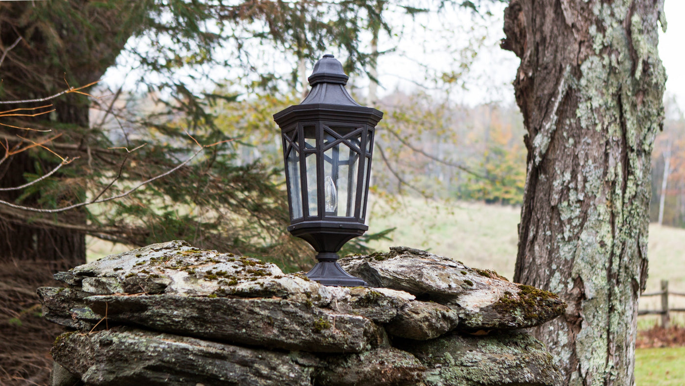 A Rockfields 21 Exterior Pier Light in Dark Waxed bronxe and glazed with clear glass, mounted on a rock wall in the Vermont countryside.