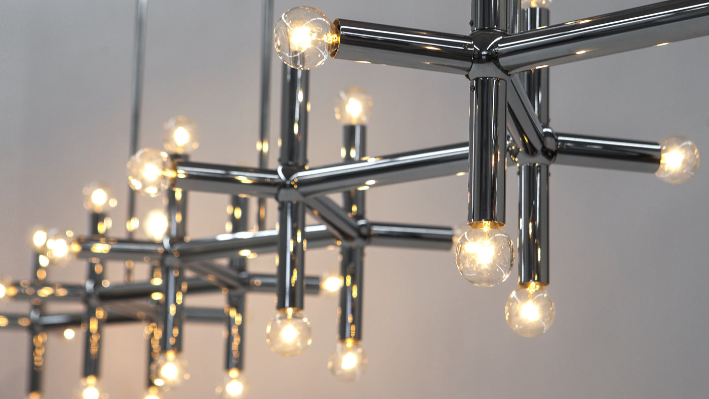 A close up photo of the Robert and Trix Haussmann Collection Molecule Linear Chandelier in Polished Nickel, showing the zig-zagging arrangement of bars and spheres of brass that comprise this lighting fixture.