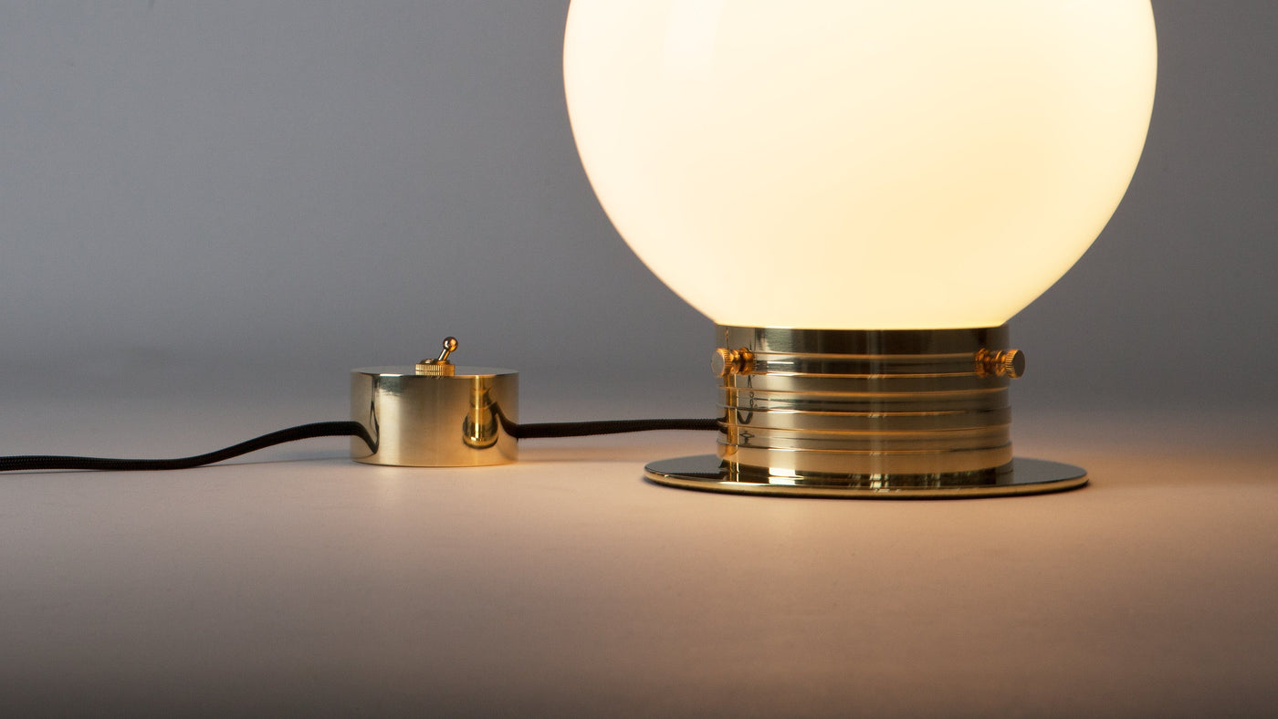 A detail of the Commune Globe Table lamp and its brass toggle switch, lit on a table and emitting warm, moody light.