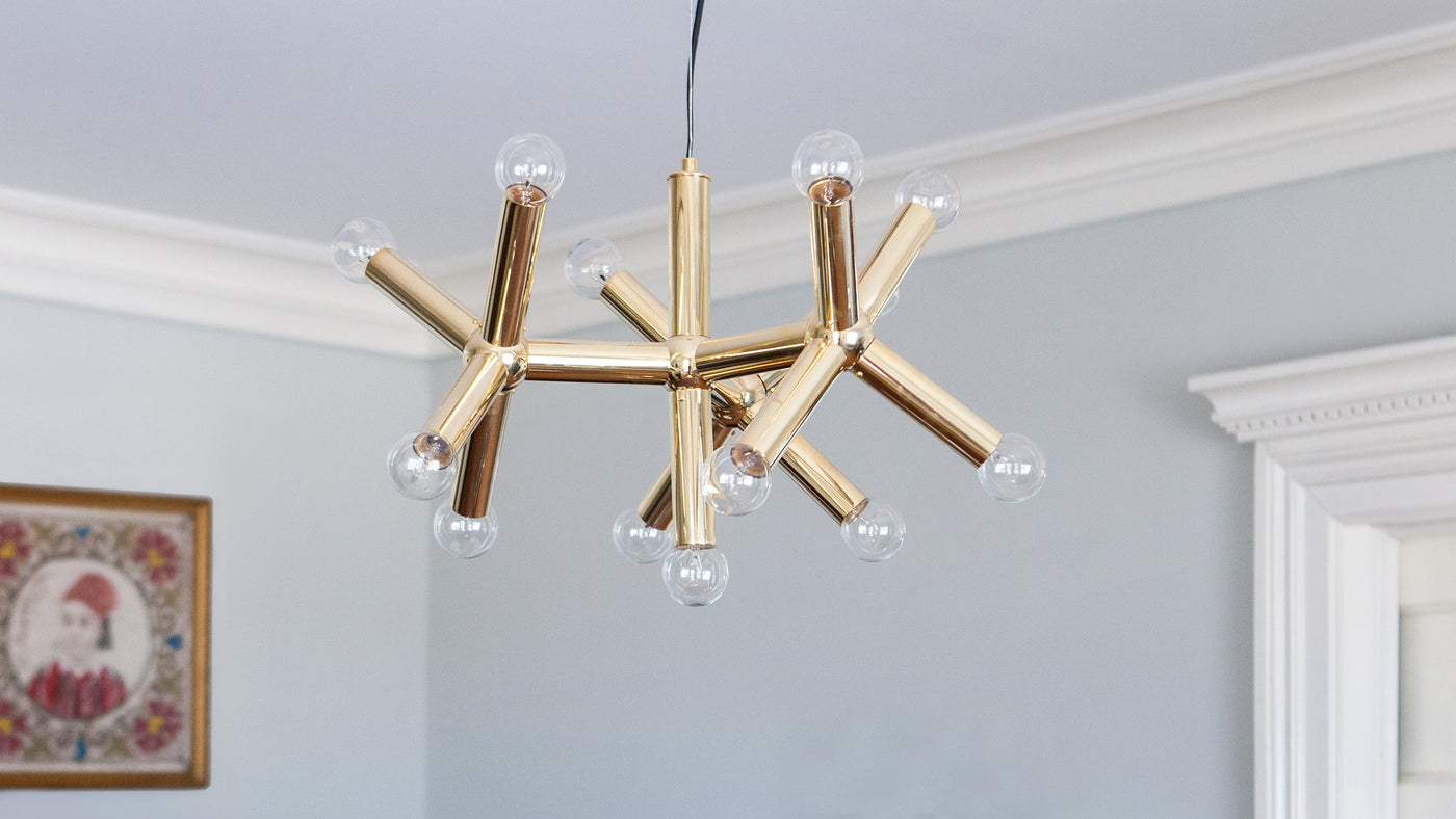 A Polished Brass Molecule Pendant, designed by Robert and Trix Haussmann and made by Remains Lighting Co., hangs in a dining room with light gray walls.