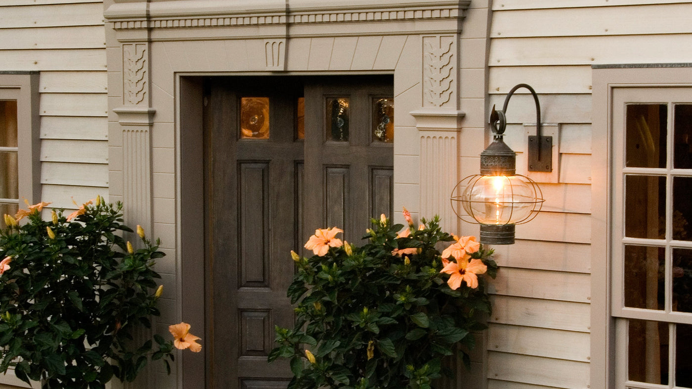 A New England Onion Exterior Wall Lantern by Scofield Lighting hangs at the entry of a clapboard country home.