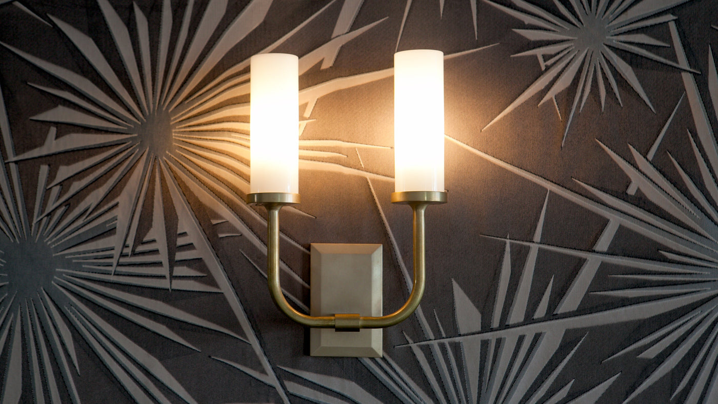 An Aloysius Twin Sconce with Glass Cylinder Shades mounted lit on Tony Duquette for Jim Thompson Fabrics in a Sunburst motif.