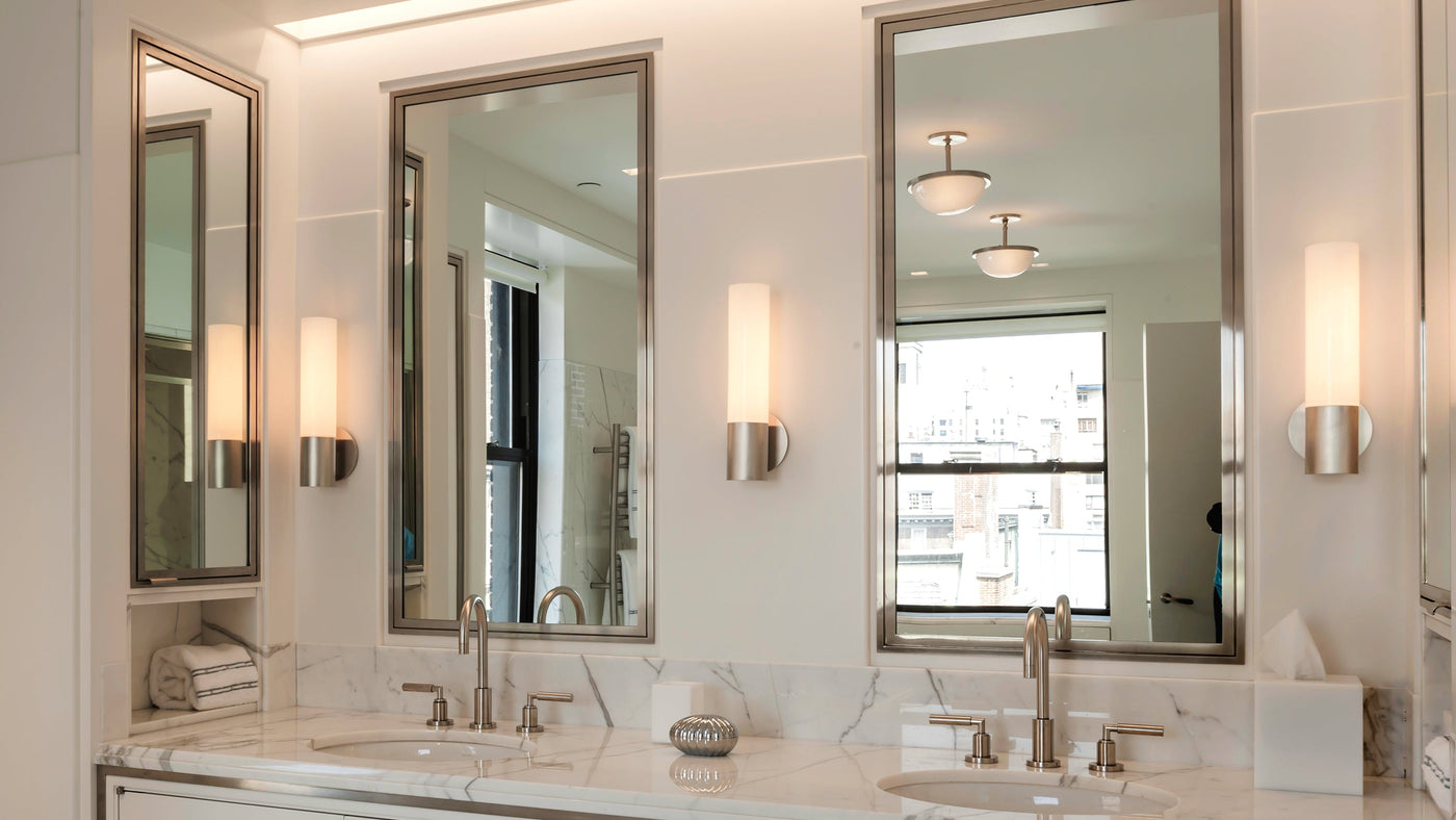 A trio of Atwater 14 sconces from Remains Lighting Co. in a satin nickel finish flank the bathroom vanity mirrors in a New York City apartment.