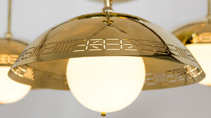 The Commune Triple Dome Chandelier consists of a trio of downward facing domes, each with the round globe inside, emerging from one central inverted bowl. This detail image features the lit globe, the mirror finish polished brass, and incised signature slash pattern.