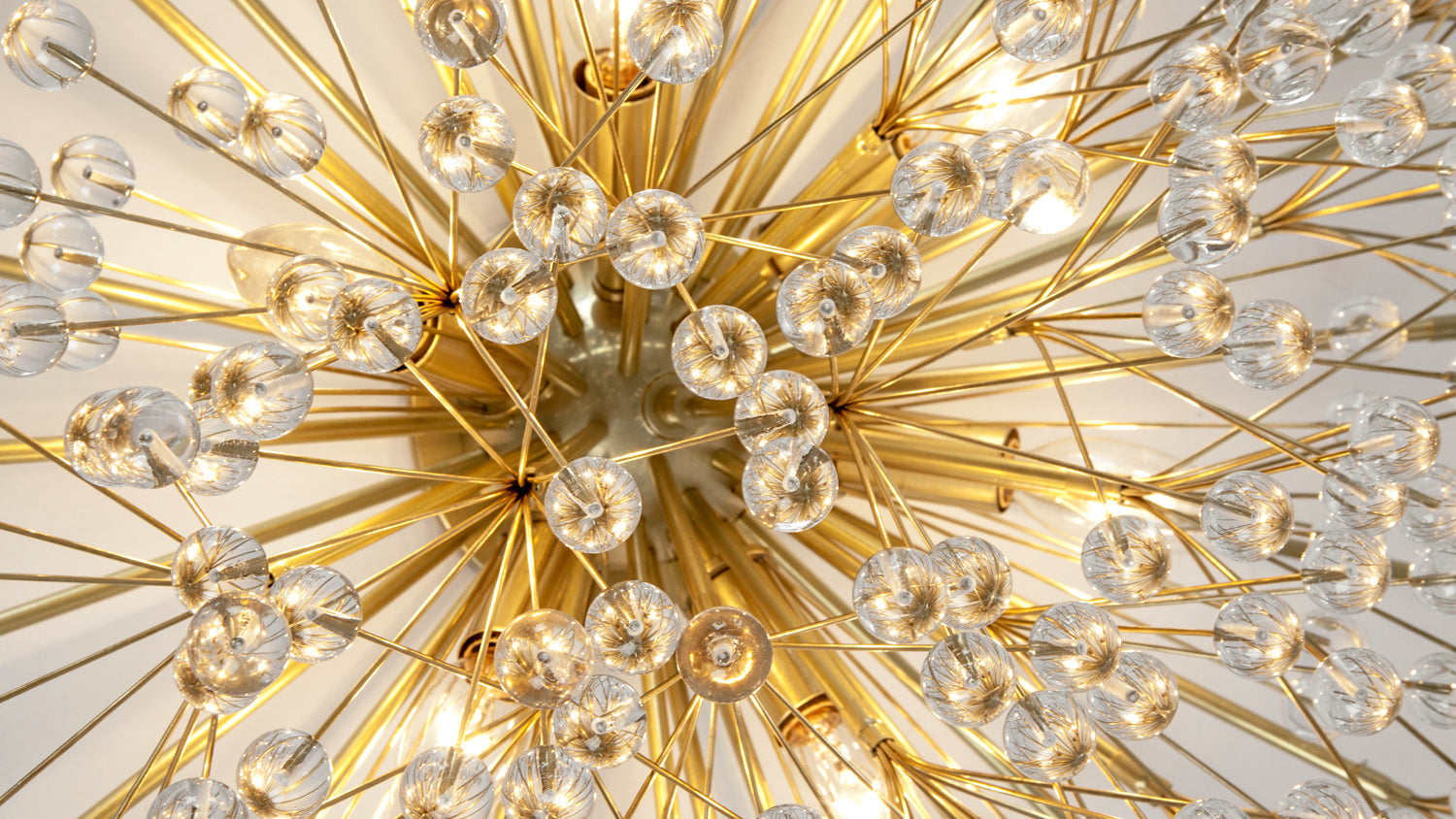 The Tony Duquette by Remains Lighting Dandelion Chandelier, its seed head seen up close and lit from within its polished brass fittings.