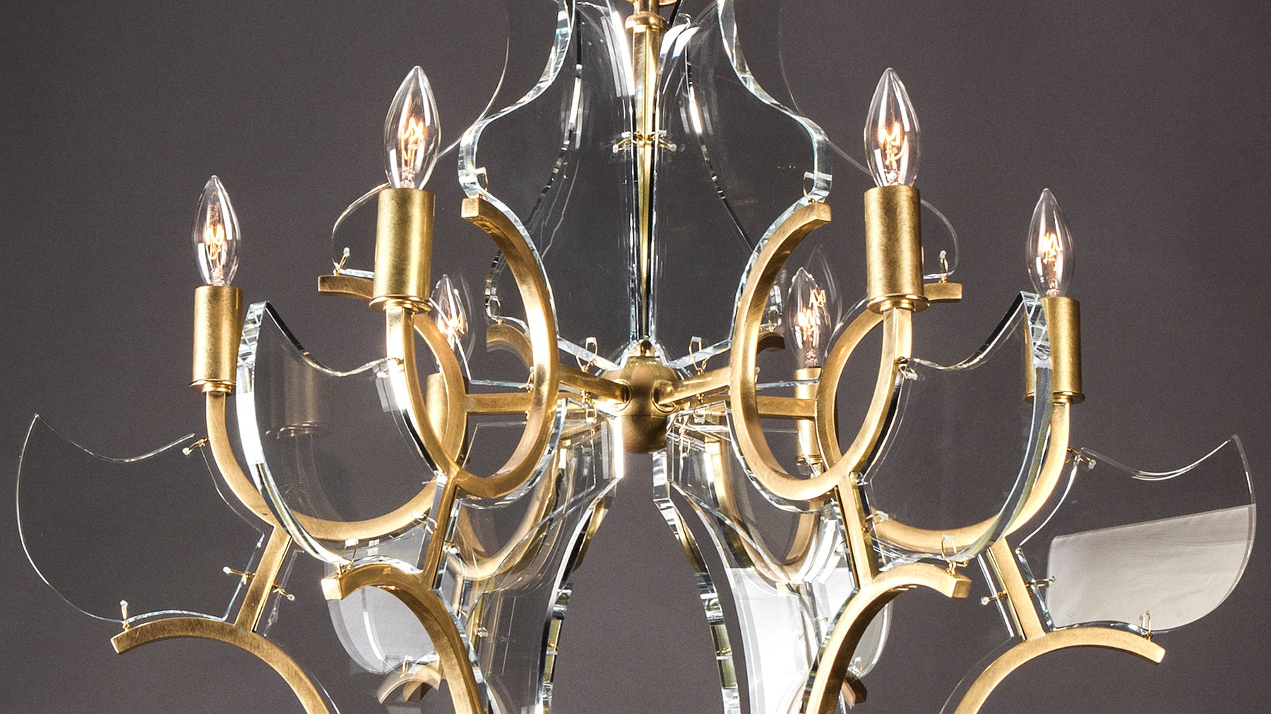 A detail shot of the Janus 12 Chandelier by Robert A.M. Stern, showing the the slightly beveled prisms of glass suspended by fine wire from square-section solid brass framing, and reflecting the light.