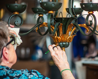 A Remains Lighting craftsperson in the work of restoring a vintage chandelier with carefully applied gilding