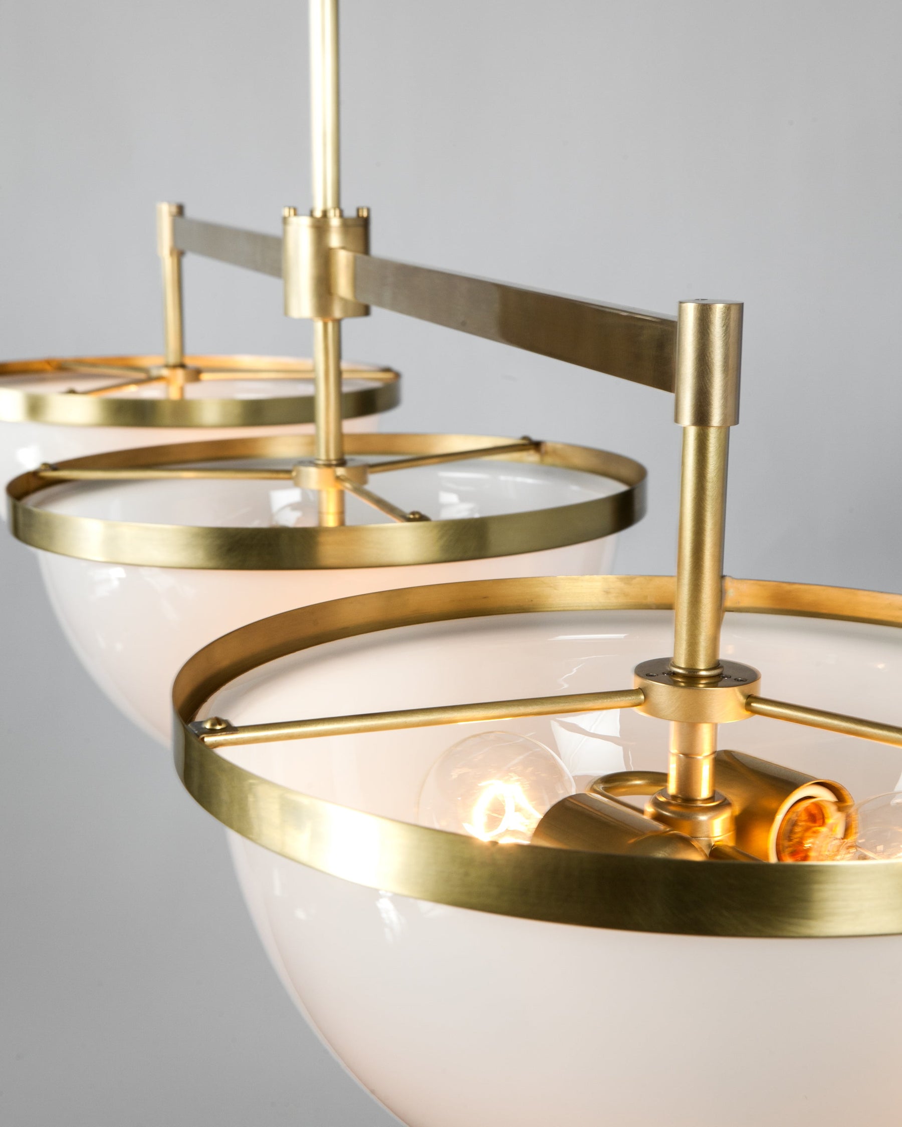 The modern brass Nevins three light billiard light viewed from above, showing the details of the rims that hold the milk glass shades and three spokes that attach the rim to the body of the fixture. The fixture is designed by Alan Wanzenberg for Remains Lighting Co.