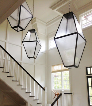 A trio of large scale, eight-sided geometric lanterns with patinated brass framing and frosted seeded glass panels hangs in a sunlit, white paneled entry hall.