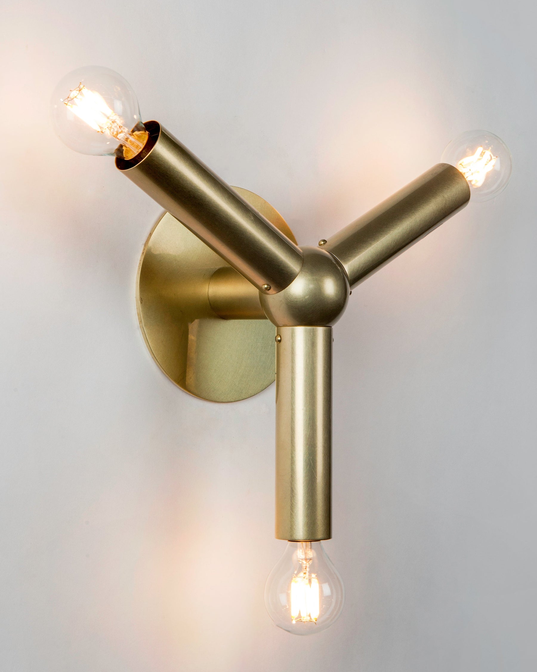 The polished brass Molecule Wall Sconce from the lighting collection by Swiss architects Robert and Trix Haussmann features a solid brass central sphere and three round bar arms, inspired by their original midcentury Atomic Lichtstruktur designs.