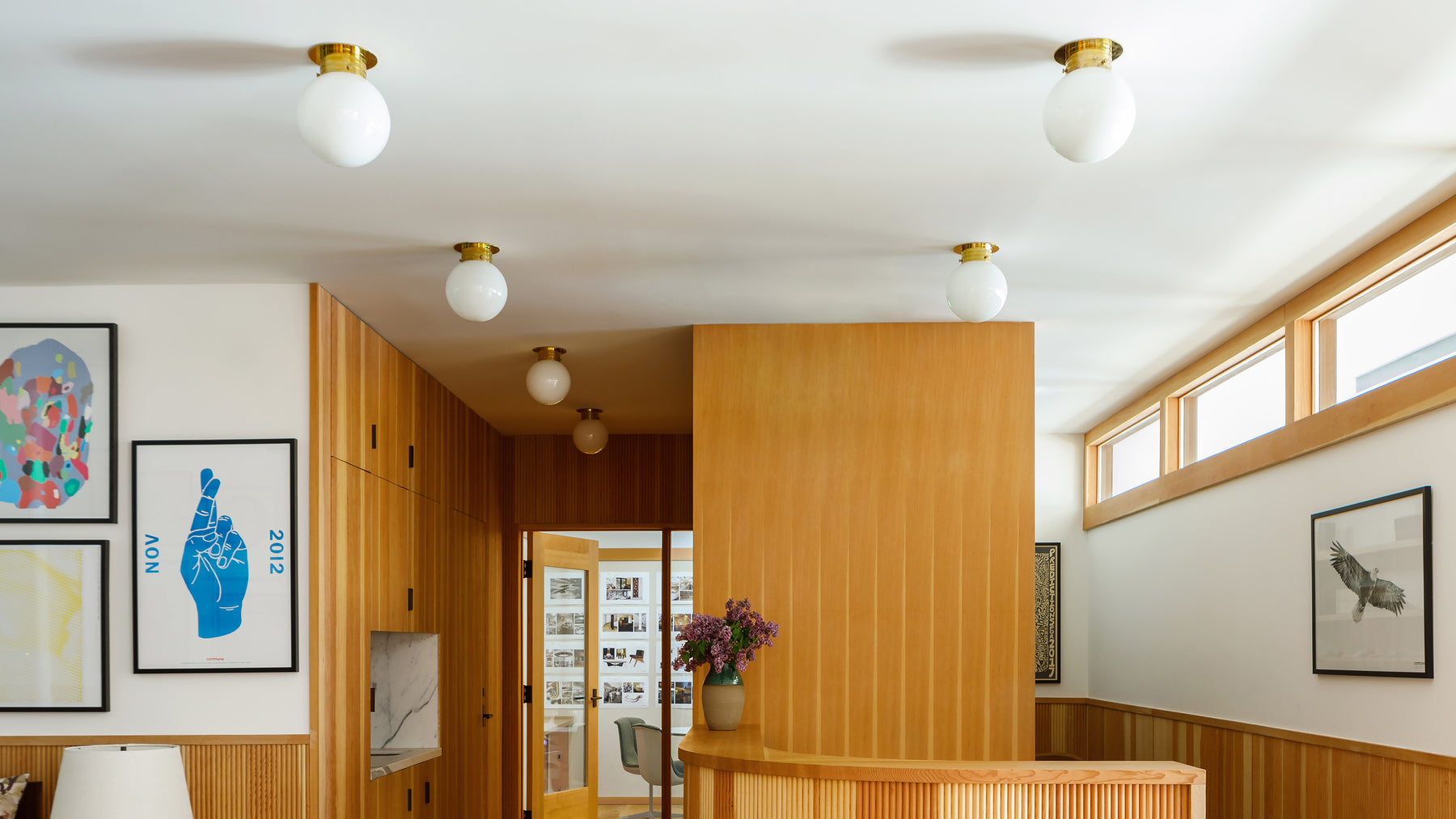 A series of Globe flush-mounted ceiling fixtures in the entry of Commune Design's LA offices, with wood paneling and artwork-lined white walls.