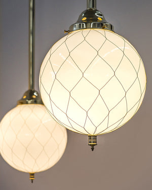 Two lit up milk-white glass Sorenson globe pendants are wrapped in handwoven wire fabric which references historical netted glass factory lighting. 