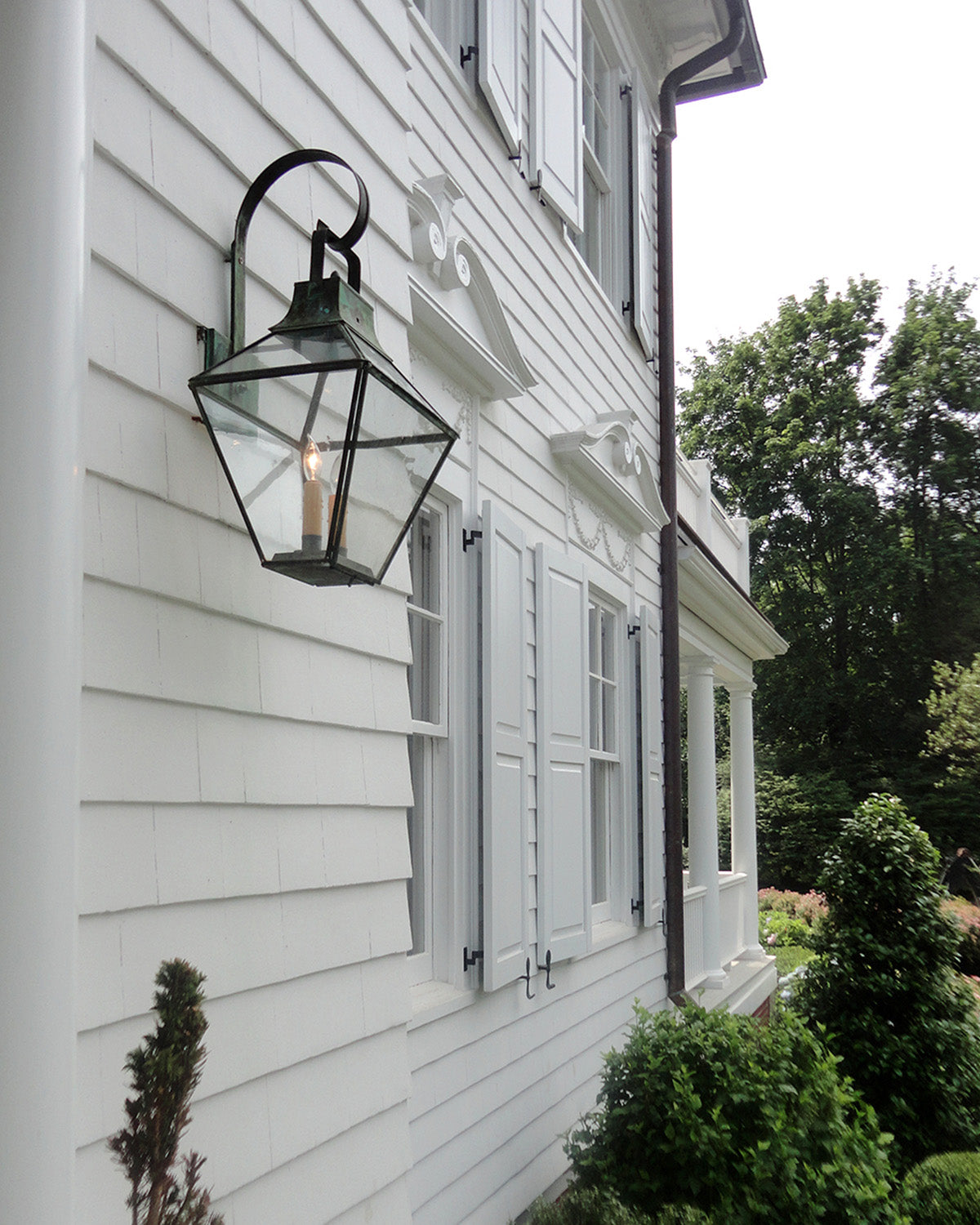 An eight-sided exterior wall lantern on a looping bracket mounted on the facade of a white clapboard home.